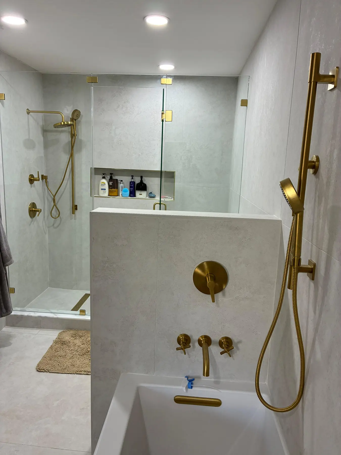 Completed walk-in shower with brushed-gold fixtures, frameless glass, and large-format stone-look tile