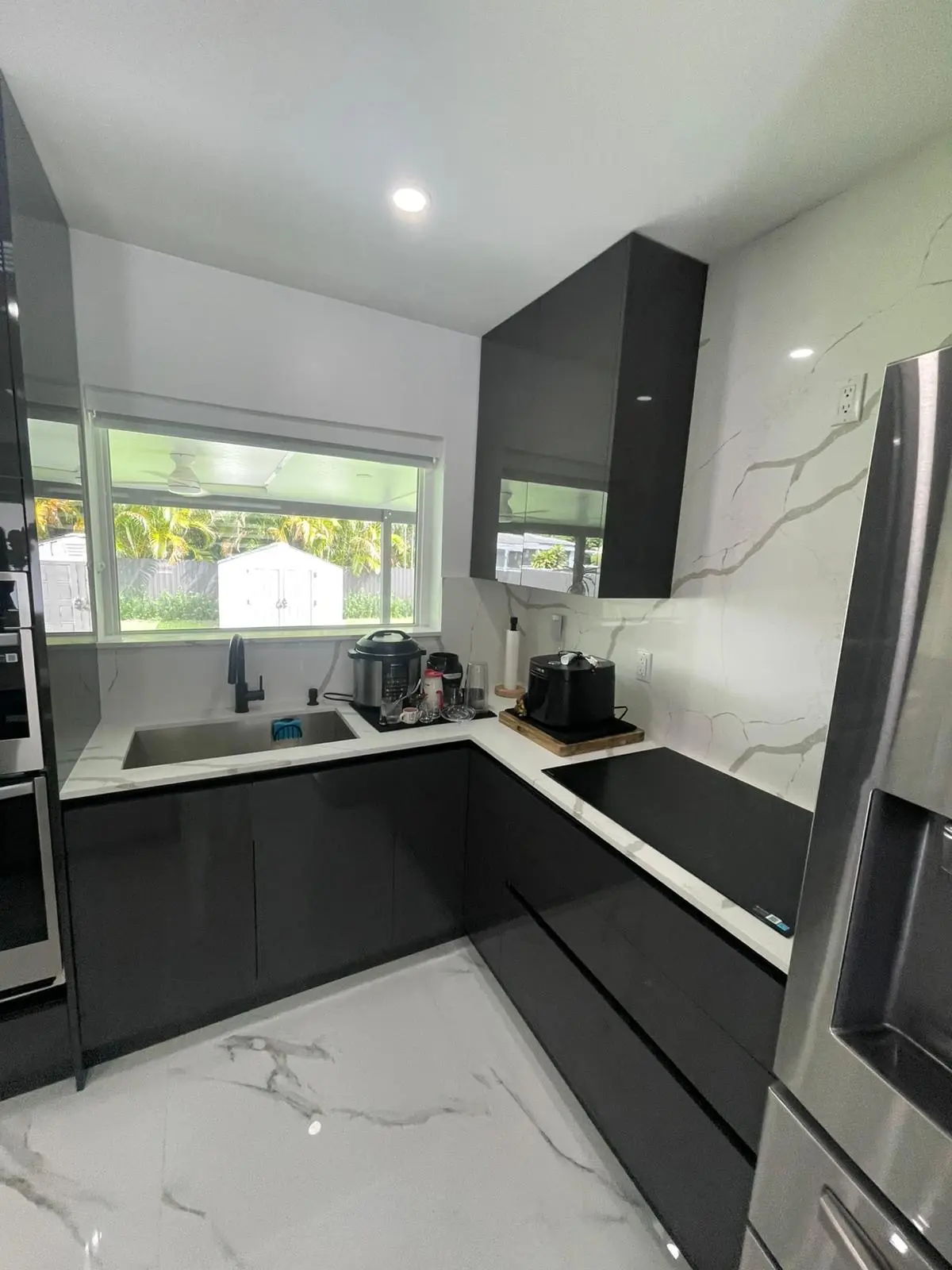 Kitchen with dark high-gloss cabinetry, a dramatic veined slab backsplash, and stone-look flooring