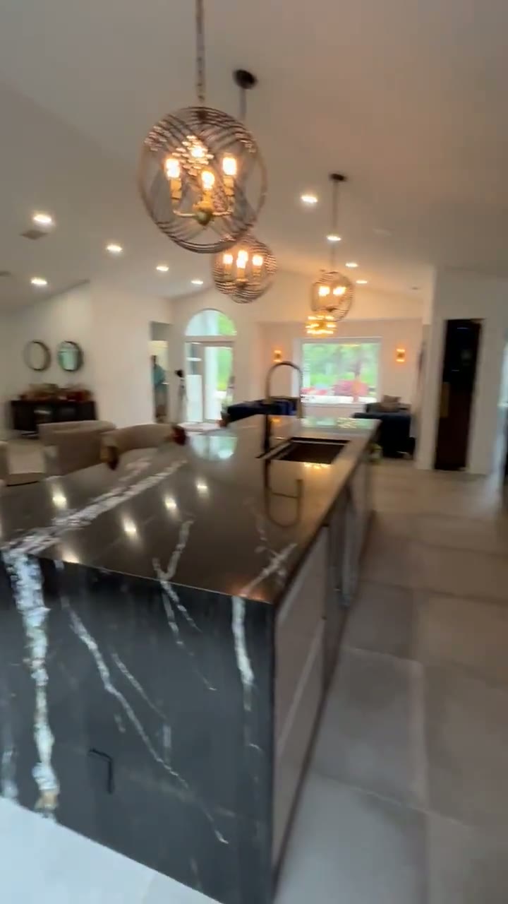 Completed kitchen with a black marble-look waterfall island and brass faucet — video preview